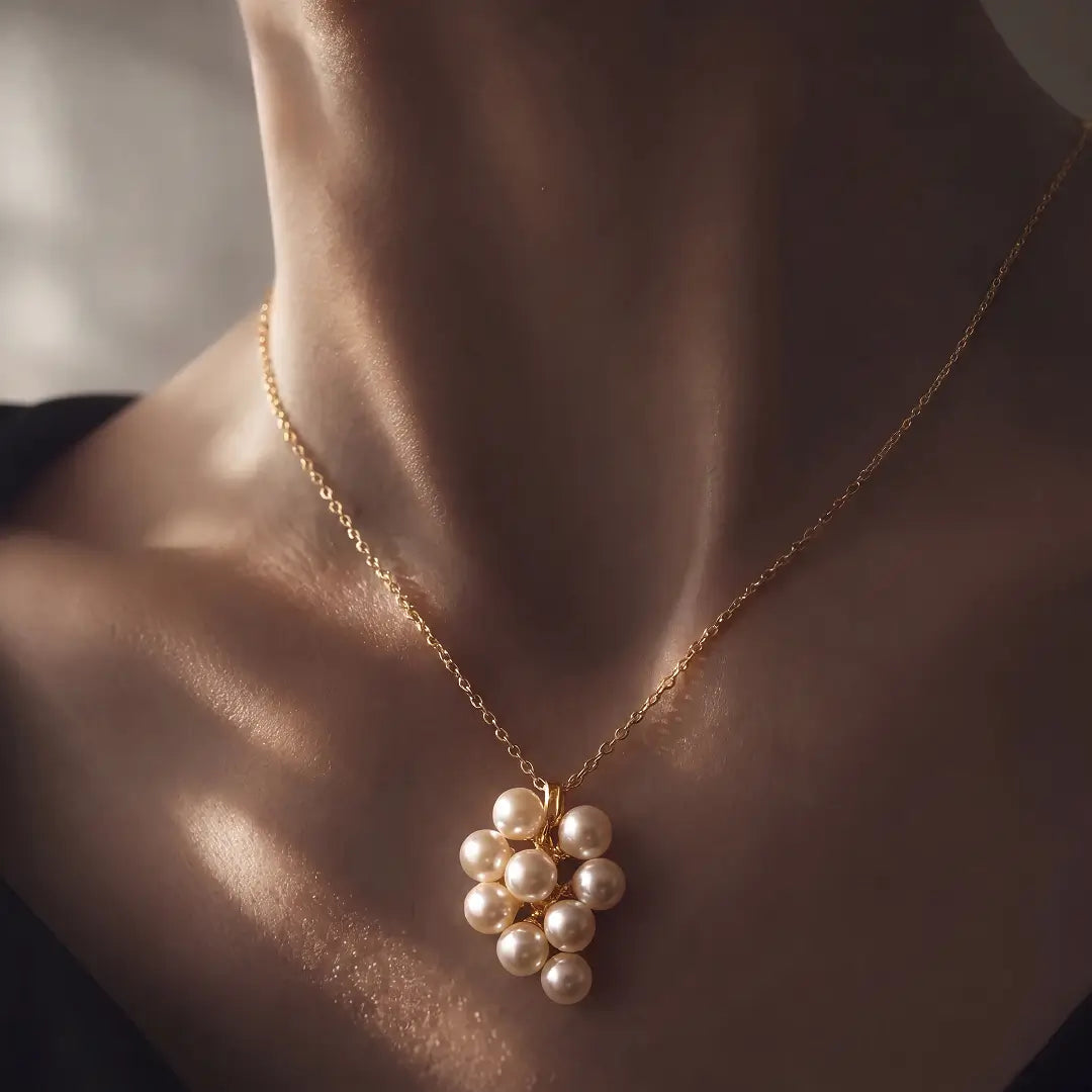 A gold chain necklace with a cluster of white pearl-like beads pendant, shown worn on a model's neck in warm, dramatic lighting.