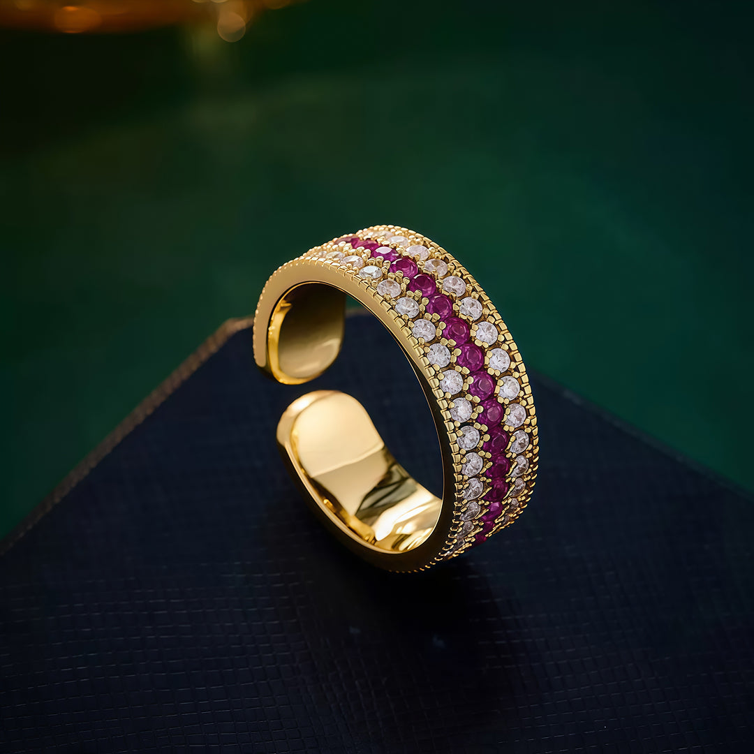 Aiko Tanaka Kiseki gold ring with rows of pink stones and white crystals displayed on a dark surface with green bokeh