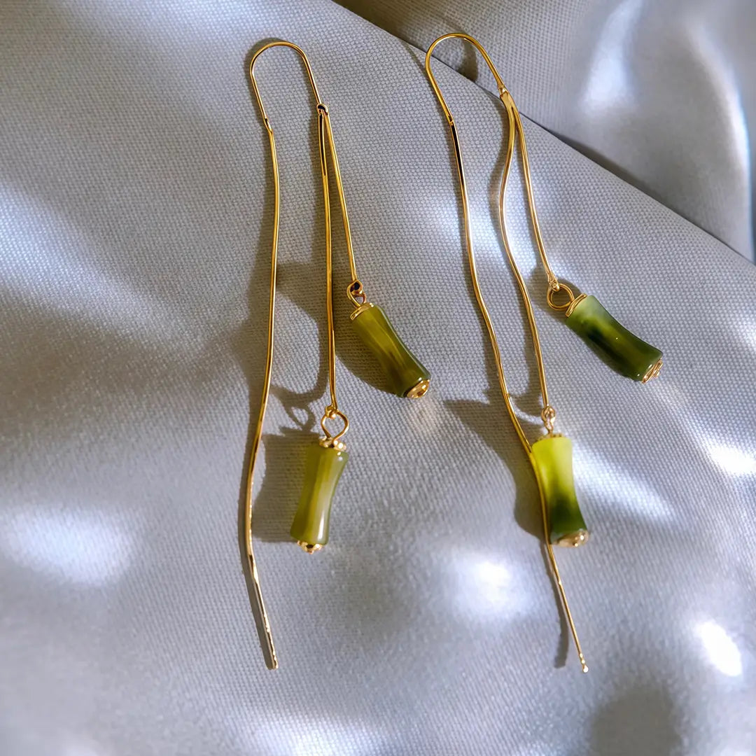 Aiko Tanaka Take no Kaze earrings, gold threaders with green bamboo drops, resting on rippled silver fabric