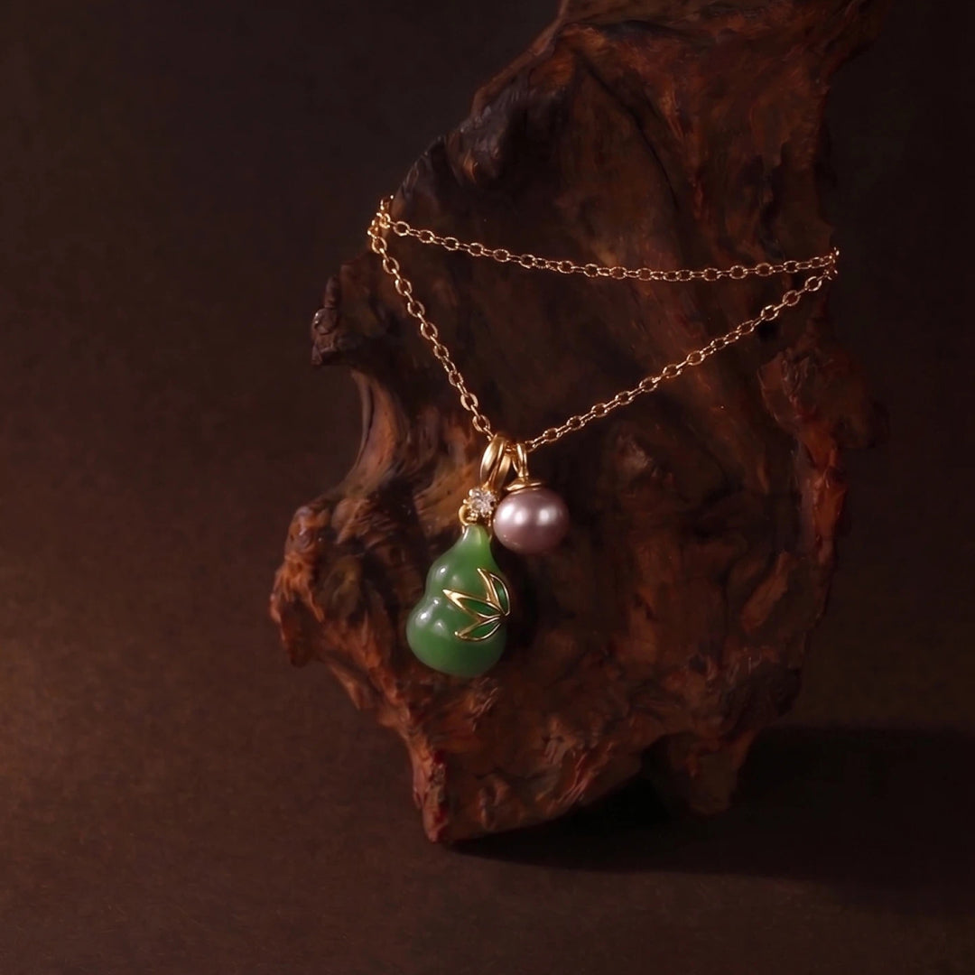 Aiko Tanaka Tsuyu no Kakera jade gourd pendant with a pink pearl on a gold chain draped over dark wood