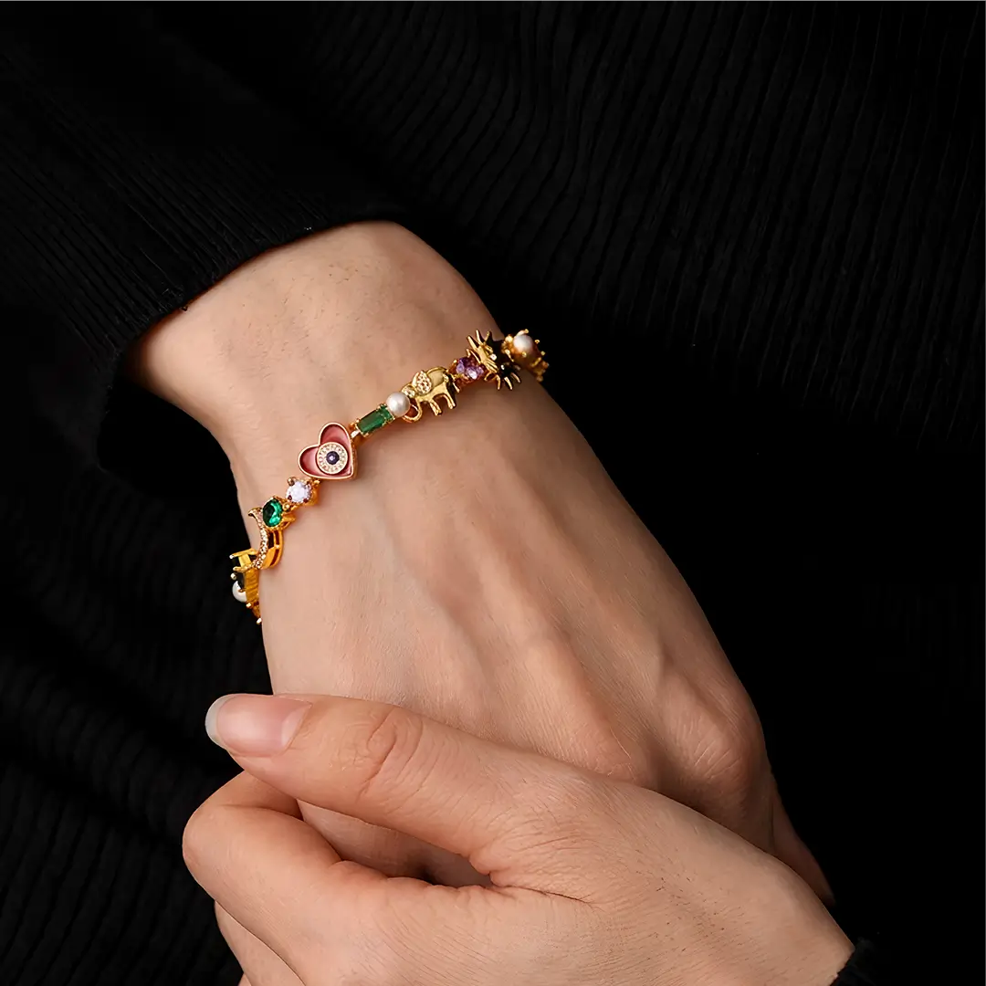 Hand adjusting the Aiko Tanaka Omamori gold bracelet with small colorful charms on a wrist against black