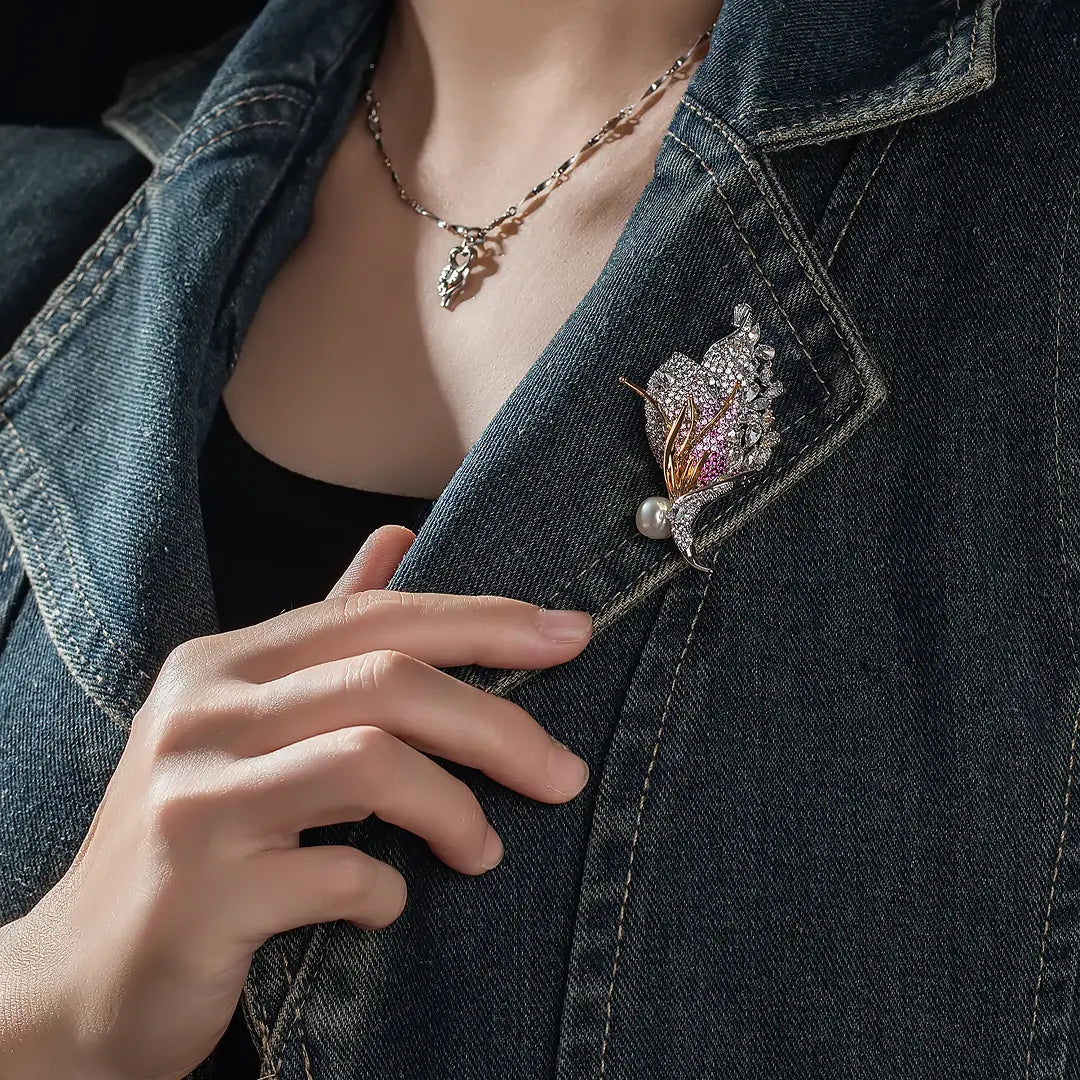 Aiko Tanaka Akatsubasa brooch, a pink and gold crystal wing with a pearl, pinned to a denim jacket on a model