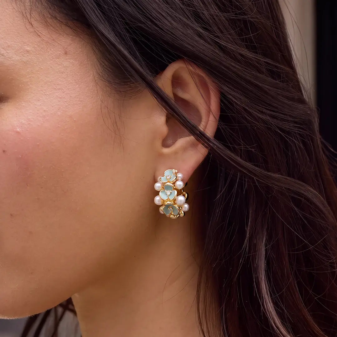 Aiko Tanaka Aonagi earrings, a gold and blue enamel flower cluster stud with pearls, worn on the ear of a model