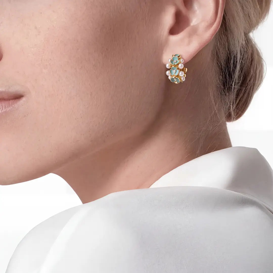 Aiko Tanaka Aonagi earrings, a blue and gold enamel flower stud with a pearl, worn on the ear with a white collar