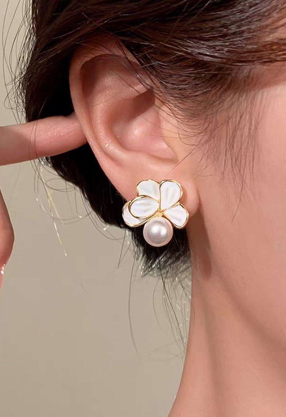 Woman touching her ear while wearing an Aiko Tanaka Kasumi Veil white enamel flower and pearl stud earring