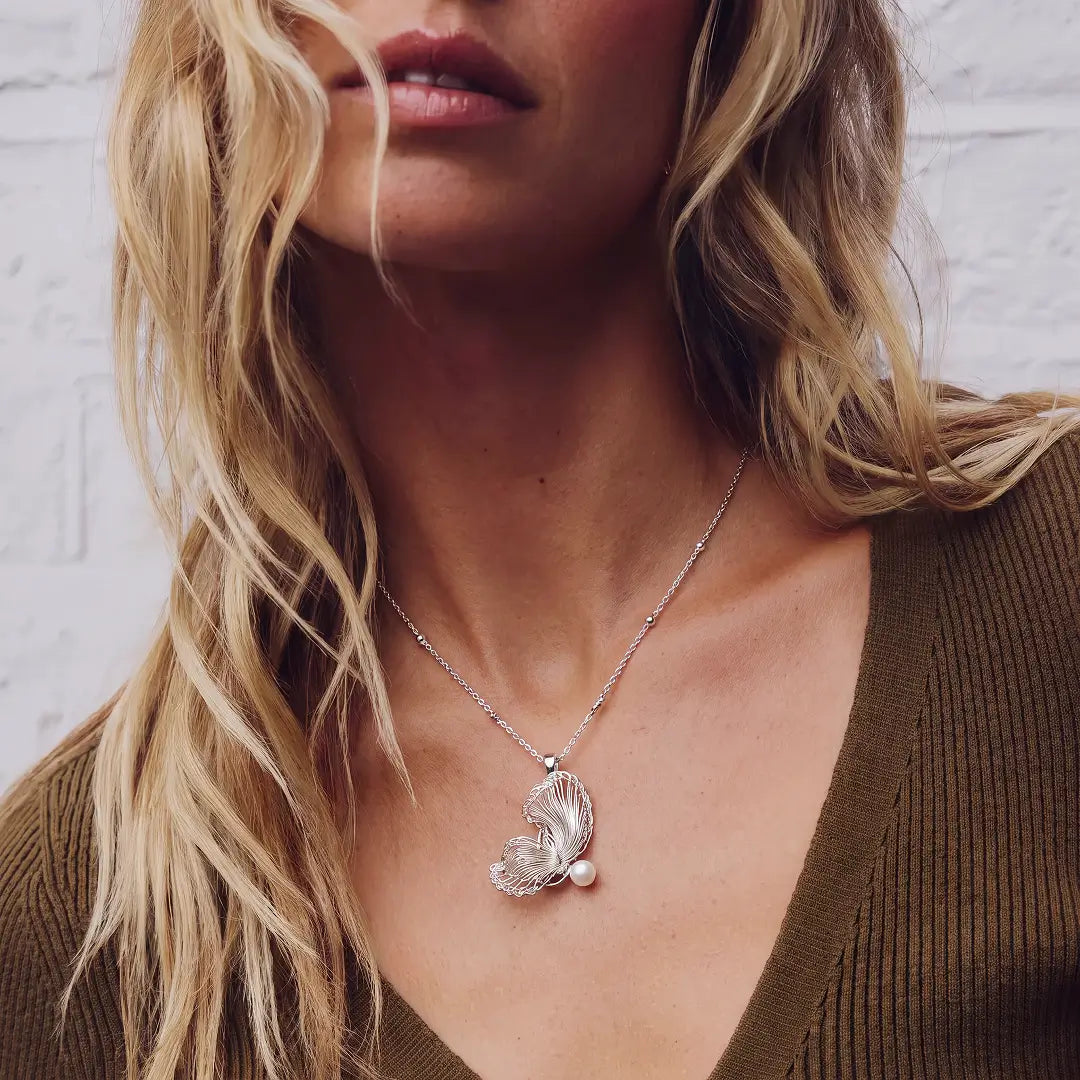 Aiko Tanaka Hakucho necklace, a silver feather wing pendant with a pearl, worn by a blonde model in a brown top