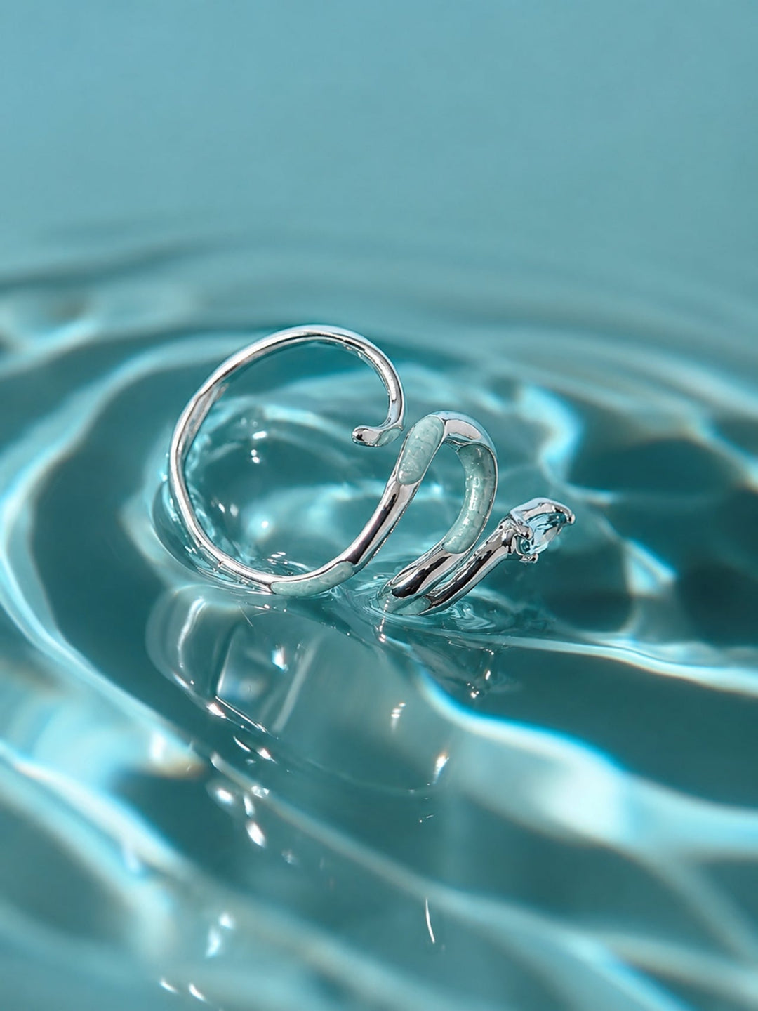 Aiko Tanaka Hebi no Nami silver snake wave ring resting in rippling aqua water, its enamel catching the light