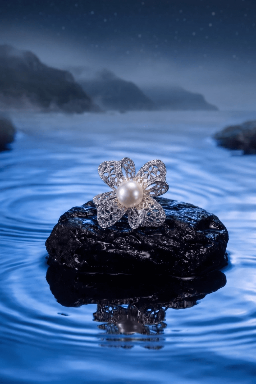 Aiko Tanaka Hikari no Hana pearl flower brooch resting on a dark rock amid rippling blue water under a night sky