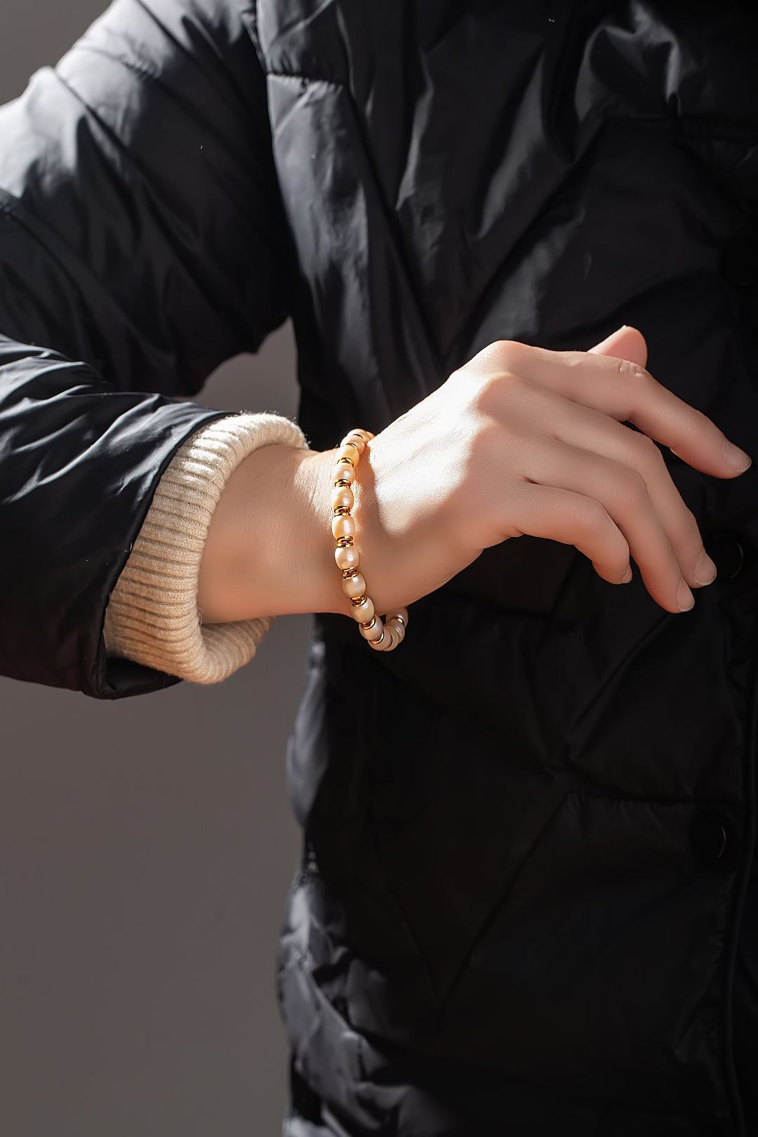 Wrist in a black puffer jacket wearing the Aiko Tanaka Hinata white pearl and gold bead bracelet
