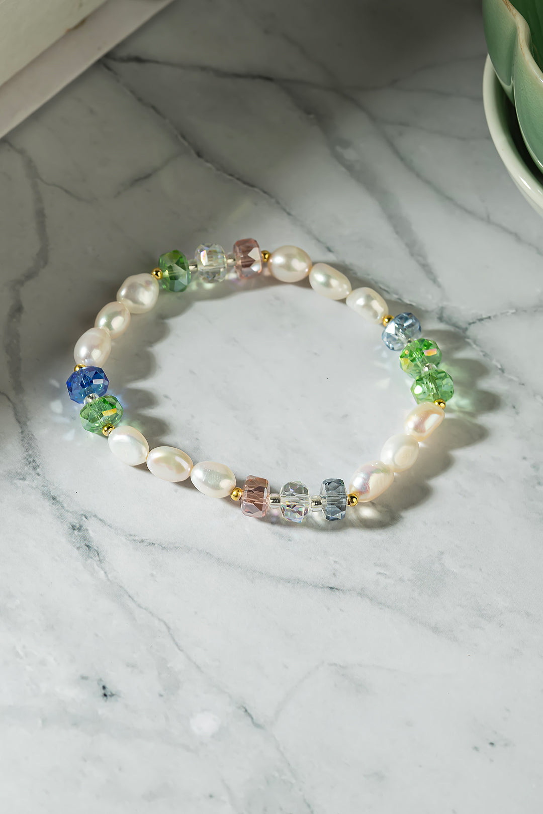 Aiko Tanaka Hoshi no Kakera bracelet of white pearls and blue, green and pink crystals laid on white marble