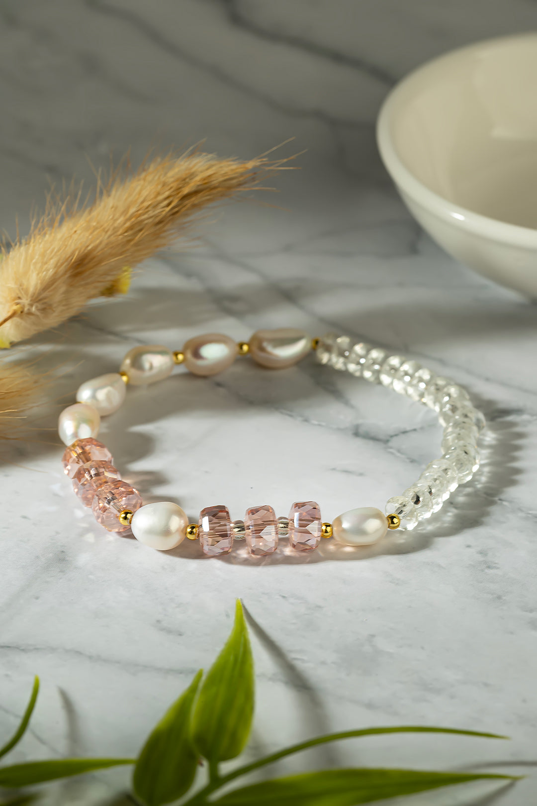 Pink Aiko Tanaka Hoshi no Kakera pearl and crystal bracelet on white marble beside a ceramic bowl and dried grass