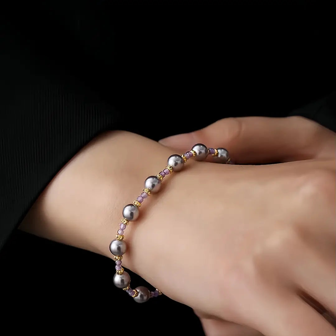 Aiko Tanaka Kasumi no Ito bracelet, a gold chain with spaced silver-grey pearls, worn on crossed wrists in black