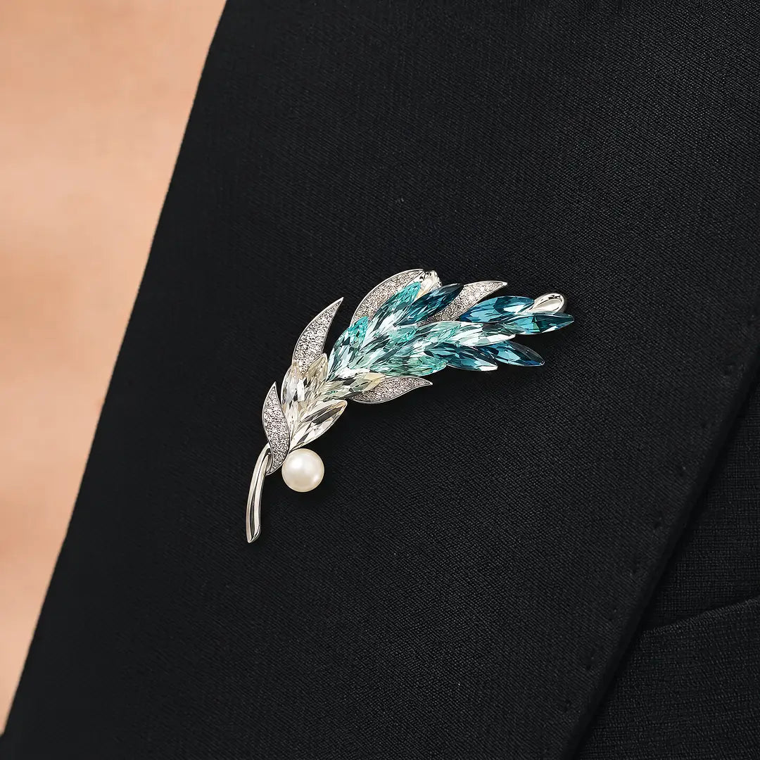 Aiko Tanaka Kazahana brooch, a teal crystal feather with a pearl, pinned to the lapel of a black blazer