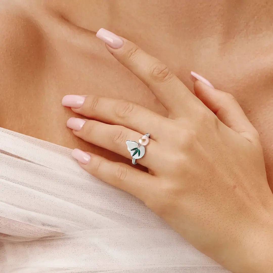 Aiko Tanaka Kissho ring on a hand resting at the chest, a silver ring with a peach pearl and white enamel gourd