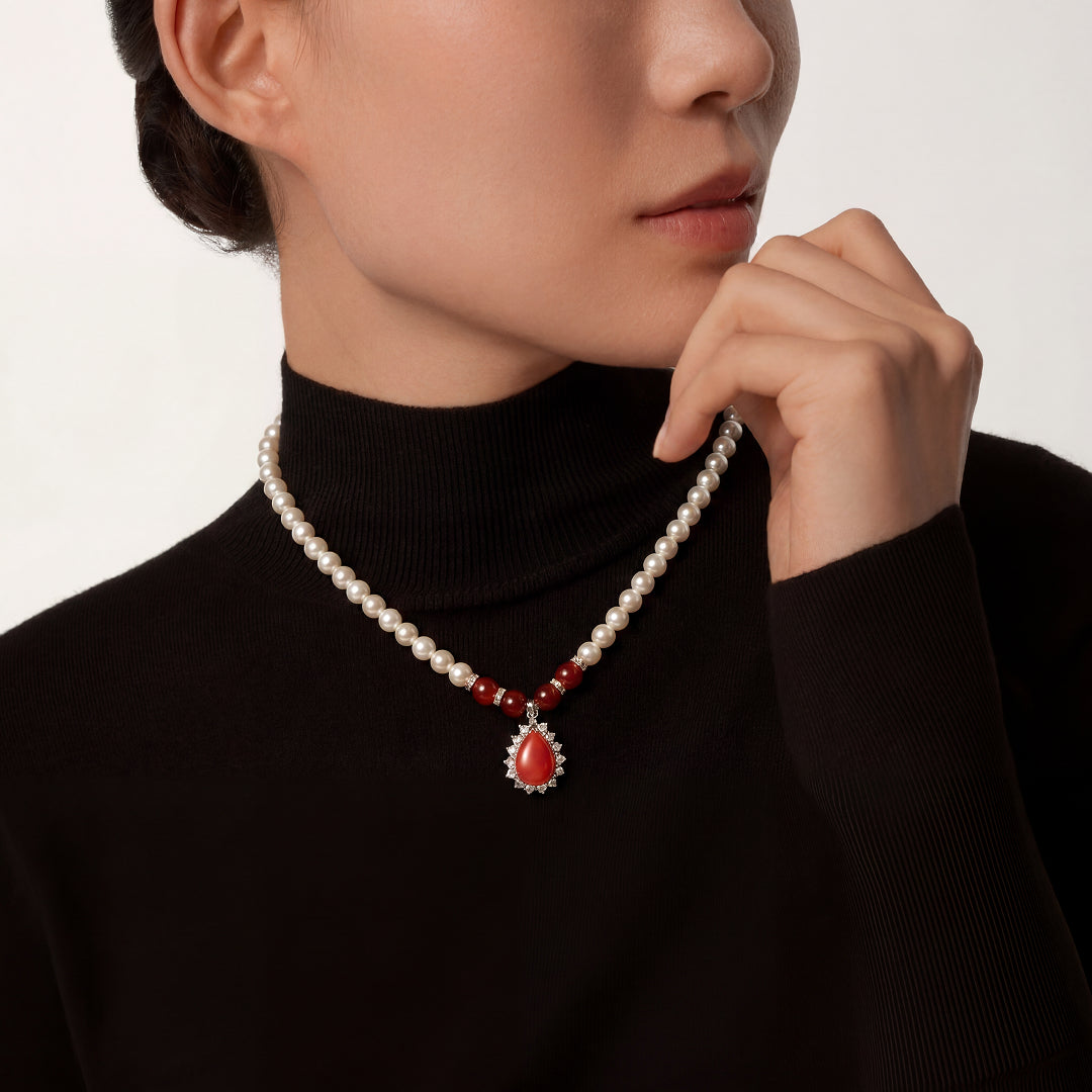 Woman in a black turtleneck touching her chin, wearing the Aiko Tanaka Kokei pearl necklace with a red drop pendant