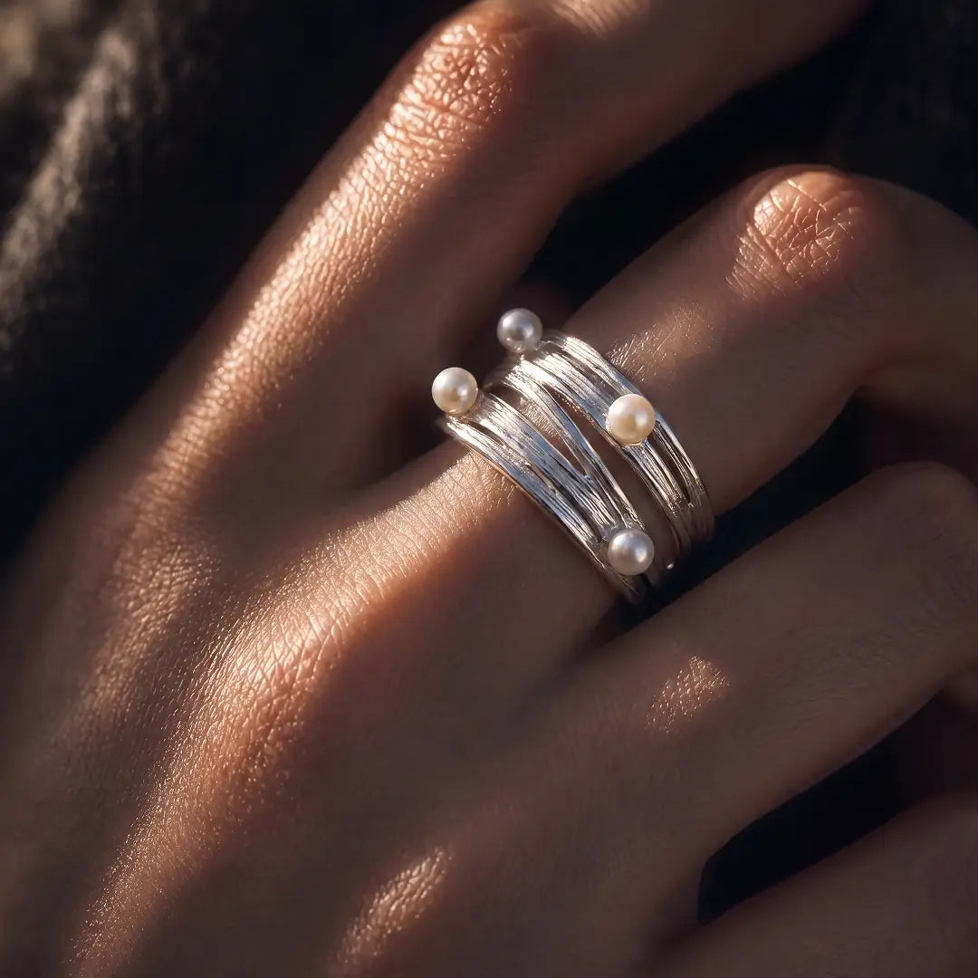 Aiko Tanaka Meguri ring, a silver multi-band wrap ring with small white pearls, worn on a finger in warm light