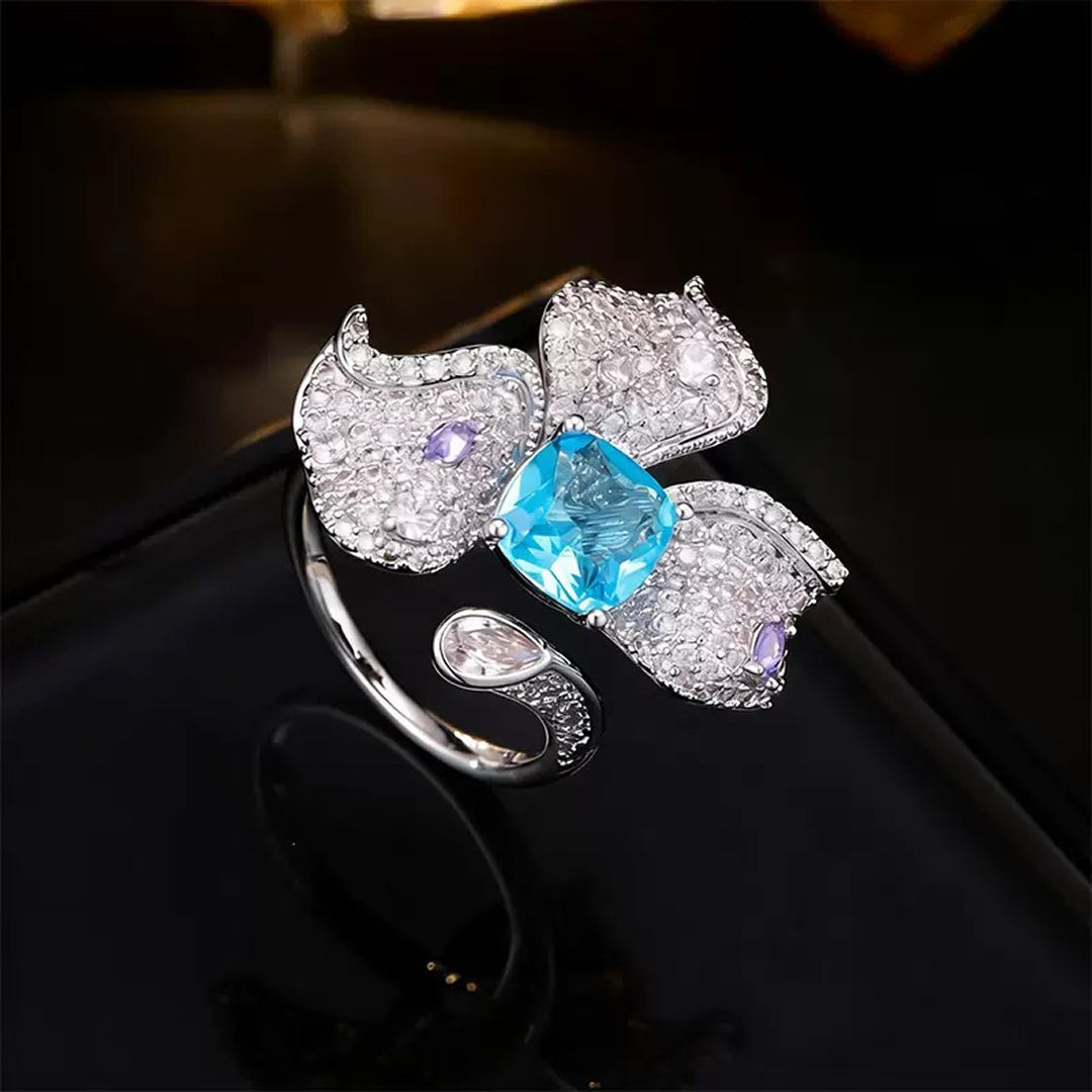 Aiko Tanaka Mizu no Ran orchid ring with lilac crystal petals and an aqua blue center stone on a dark background