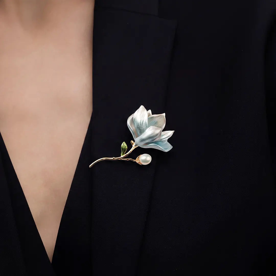 Aiko Tanaka Mizuhana brooch, a blue enamel magnolia with a pearl bud, worn on a black V-neck top