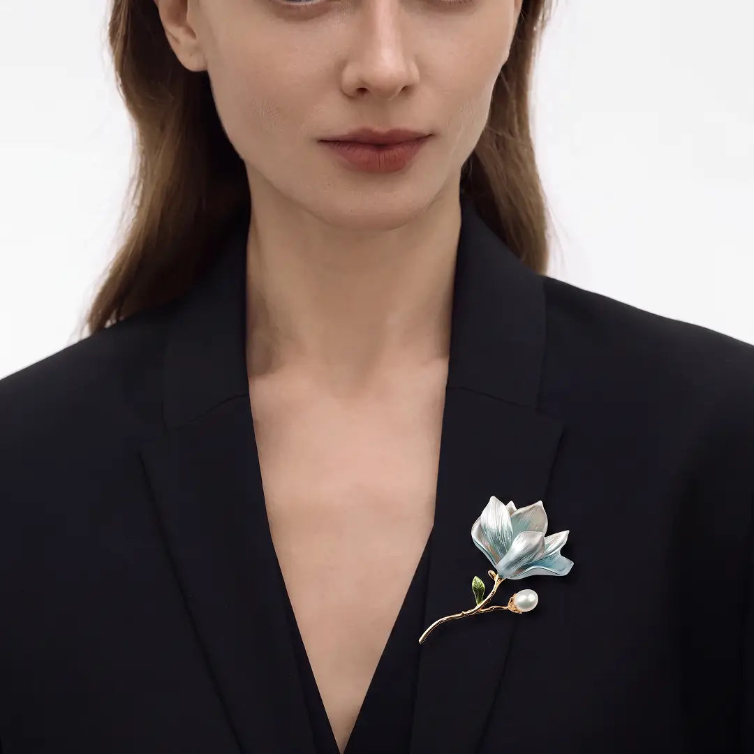 Aiko Tanaka Mizuhana brooch, a pale blue enamel magnolia with a pearl, pinned to a black blazer worn by a model