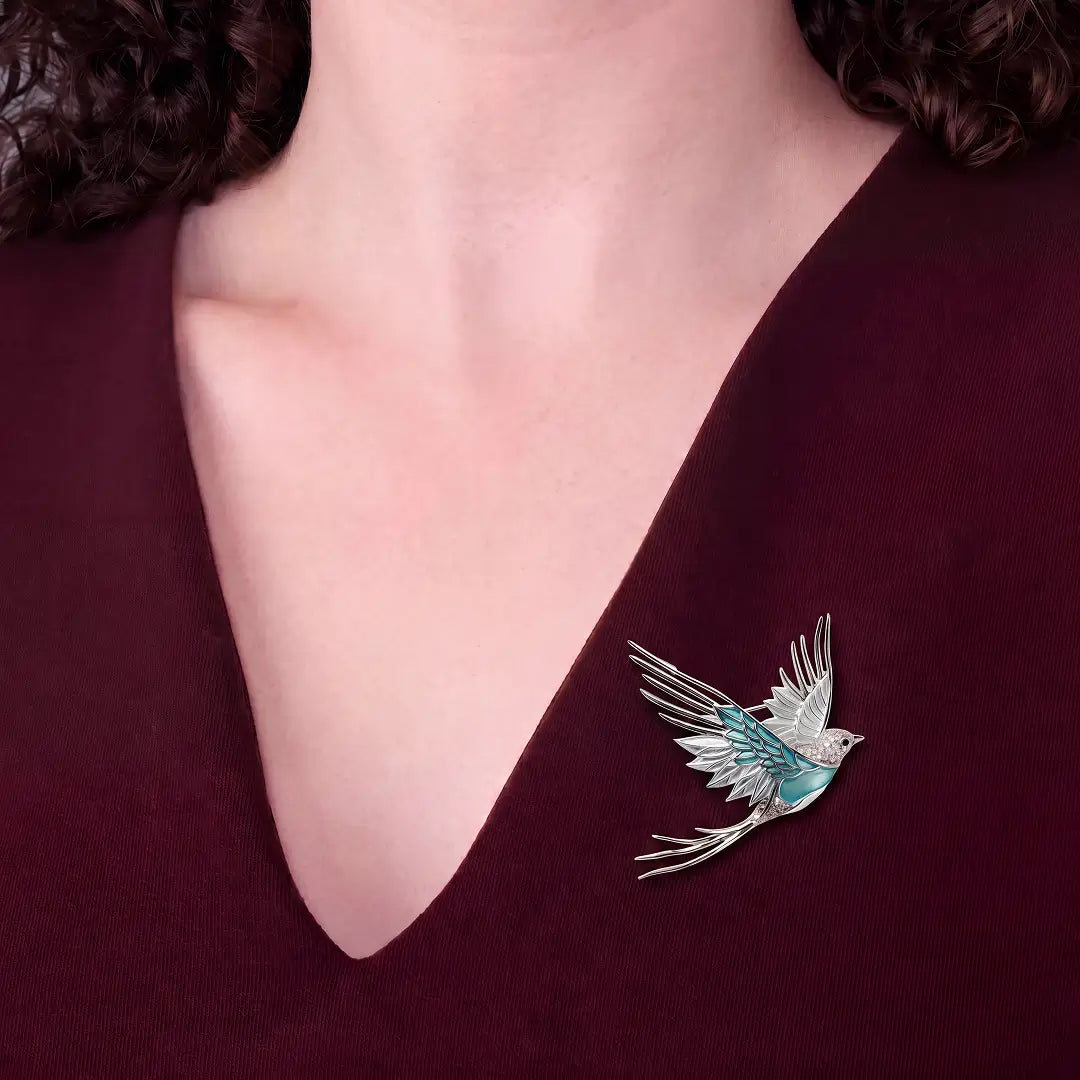 Woman in a burgundy V-neck wearing the Aiko Tanaka Mizuhane silver and teal enamel bird brooch