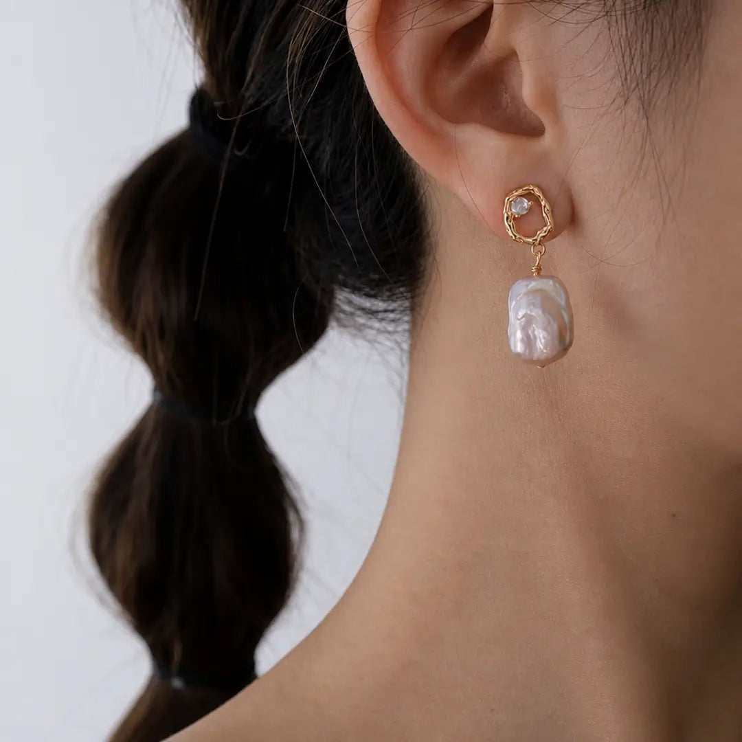 Aiko Tanaka Nagori earrings, a baroque pearl drop below a small gold-framed stone, worn by a model with braids