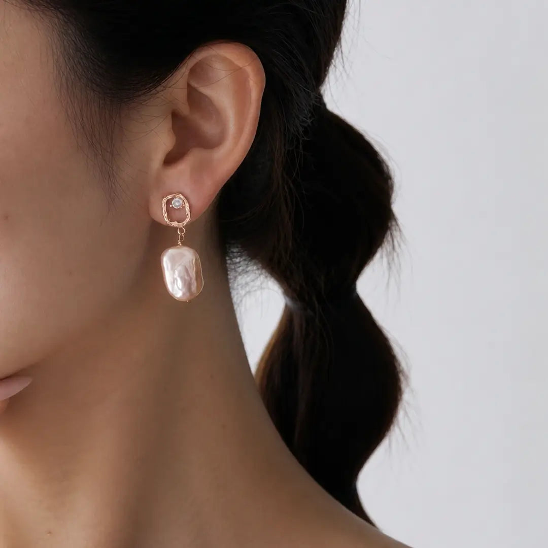 Aiko Tanaka Nagori earrings worn on the ear, a long baroque pearl hanging from a rose gold stud, braided hair