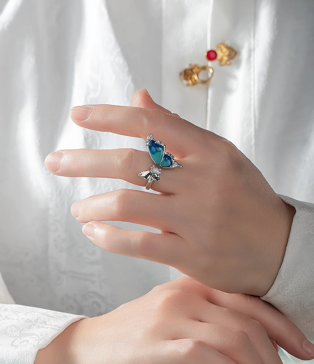 Hand in a white embroidered shirt wearing the Aiko Tanaka Ran no Cho blue enamel butterfly ring on the index finger