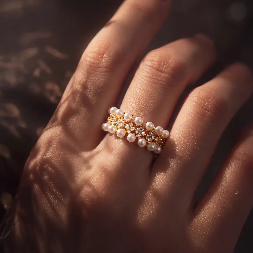 Aiko Tanaka Rinka ring, a gold pearl cluster ring, worn on the hand in warm light with shadows across the skin