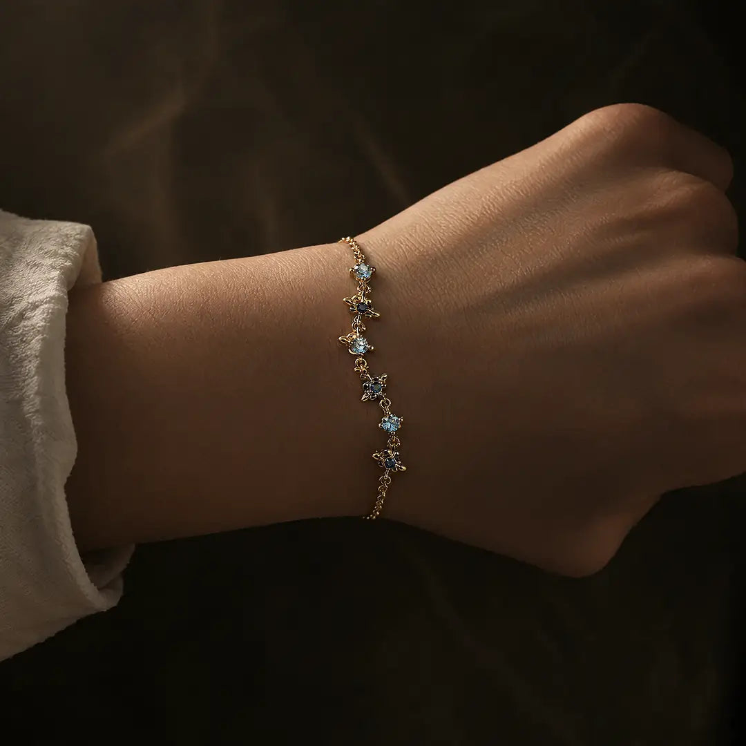 Aiko Tanaka Sazanami bracelet, a delicate gold chain with tiny blue stone flowers, worn on the wrist in low light
