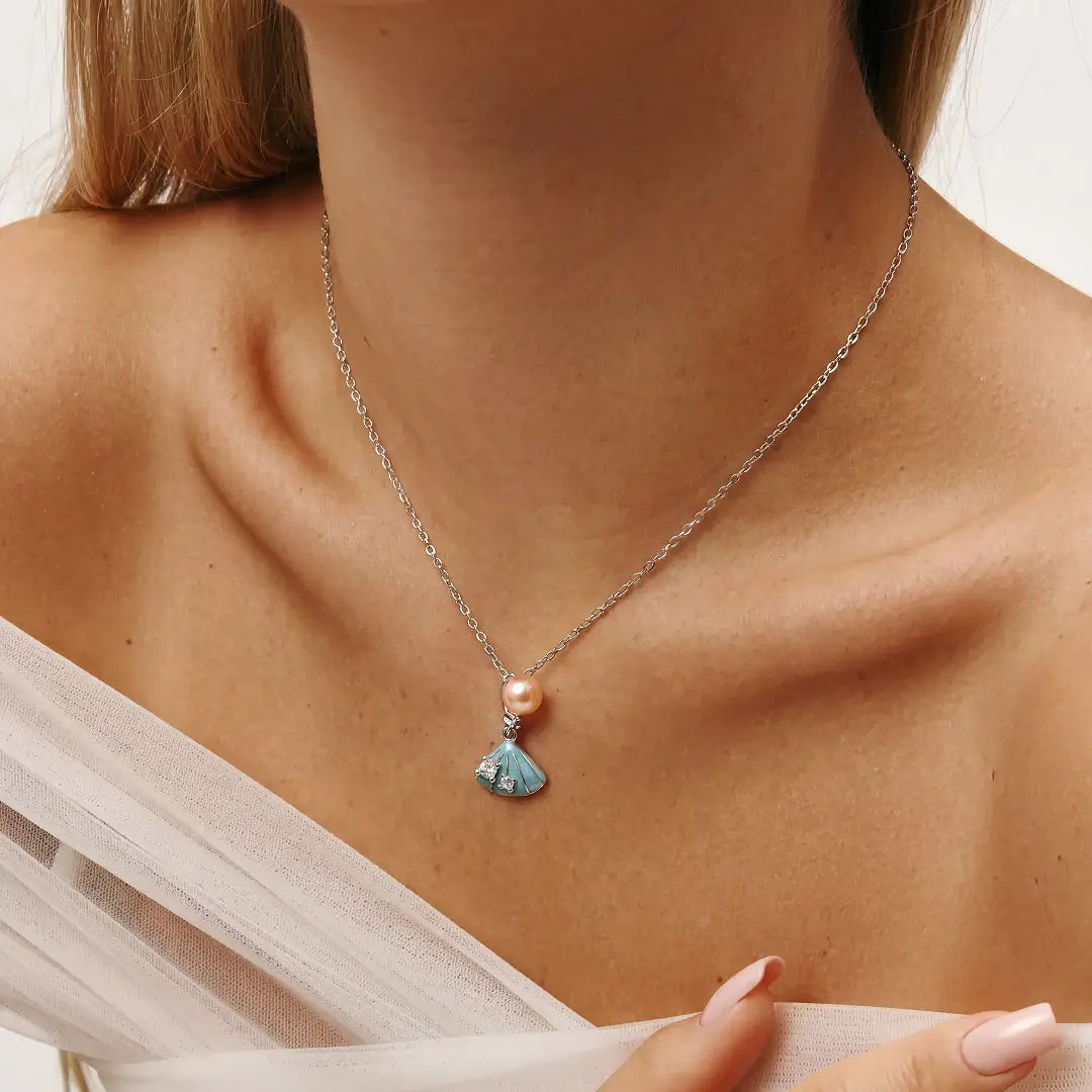 Aiko Tanaka Suiren necklace, a peach pearl and blue enamel lily pad pendant, worn with an off-shoulder white top