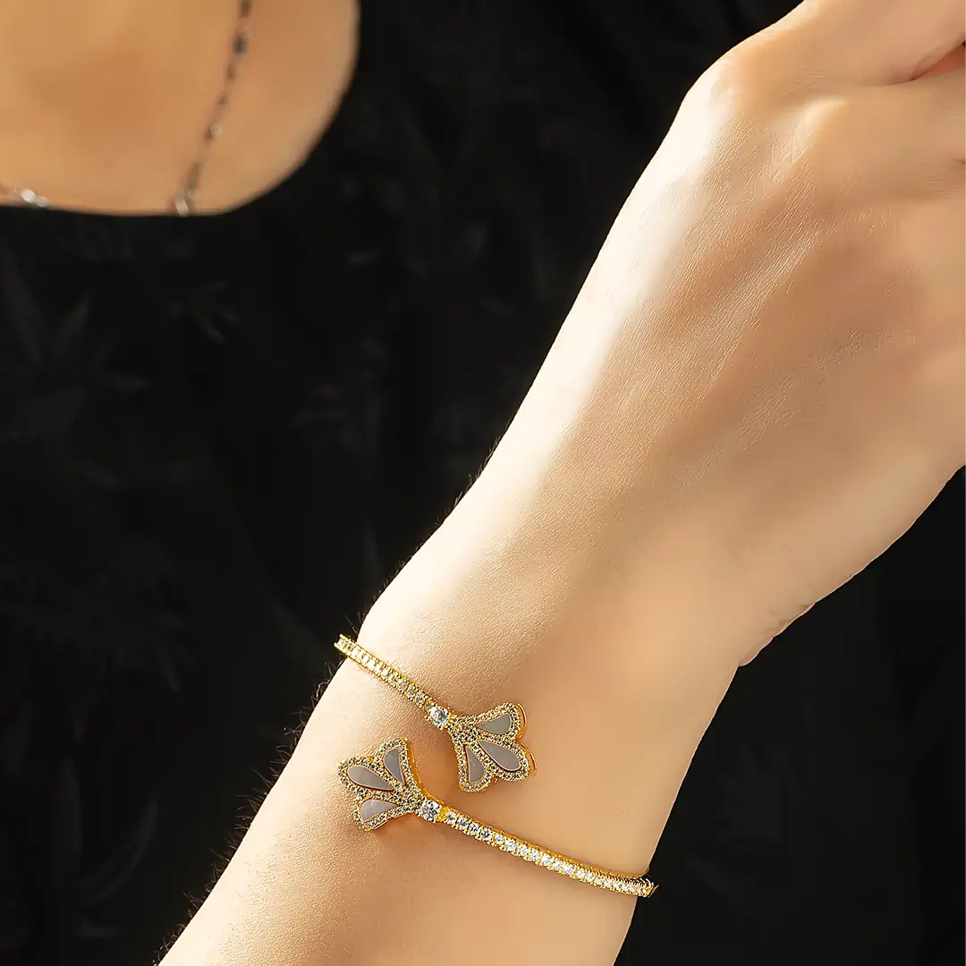 Aiko Tanaka Yohaku bracelet, a gold cuff with crystal ginkgo leaf ends, worn on the wrist against a black top