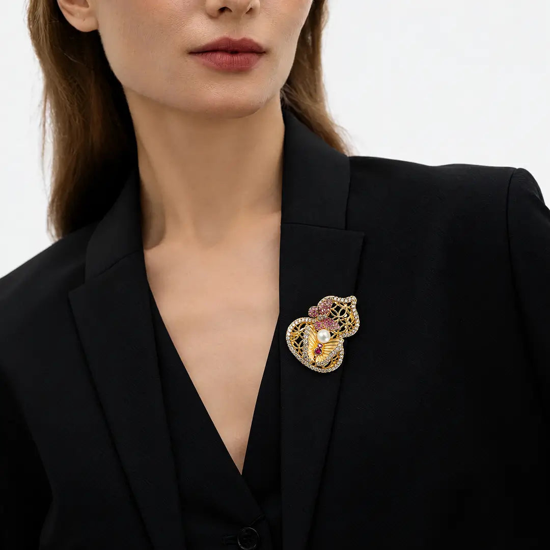 Aiko Tanaka Yugen brooch, a gold gourd with pink flowers and a pearl, pinned to a black blazer on a model